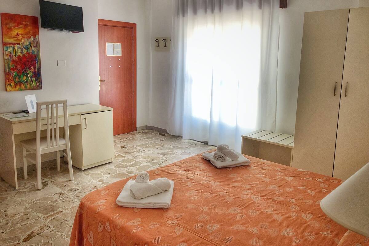 Ein Hotelzimmer mit Bett, Schreibtisch, Stuhl, Kleiderschrank, Fernseher und einem Fenster mit Vorhängen.