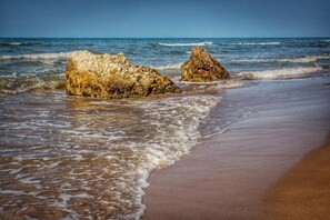 A beach with two prominent rocks and waves approaching the shore.