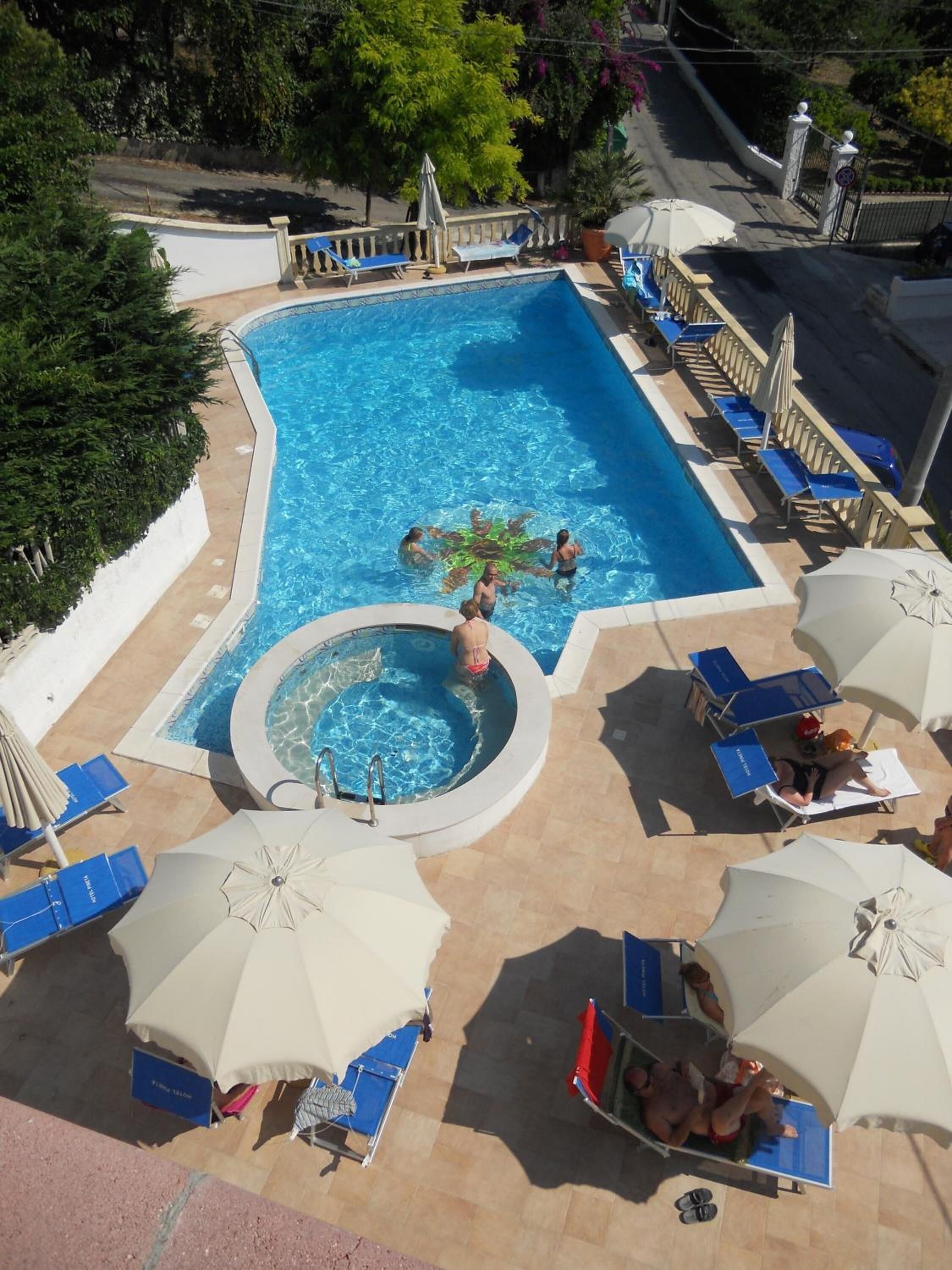 Une piscine avec un jacuzzi, entourée de chaises longues et de parasols.