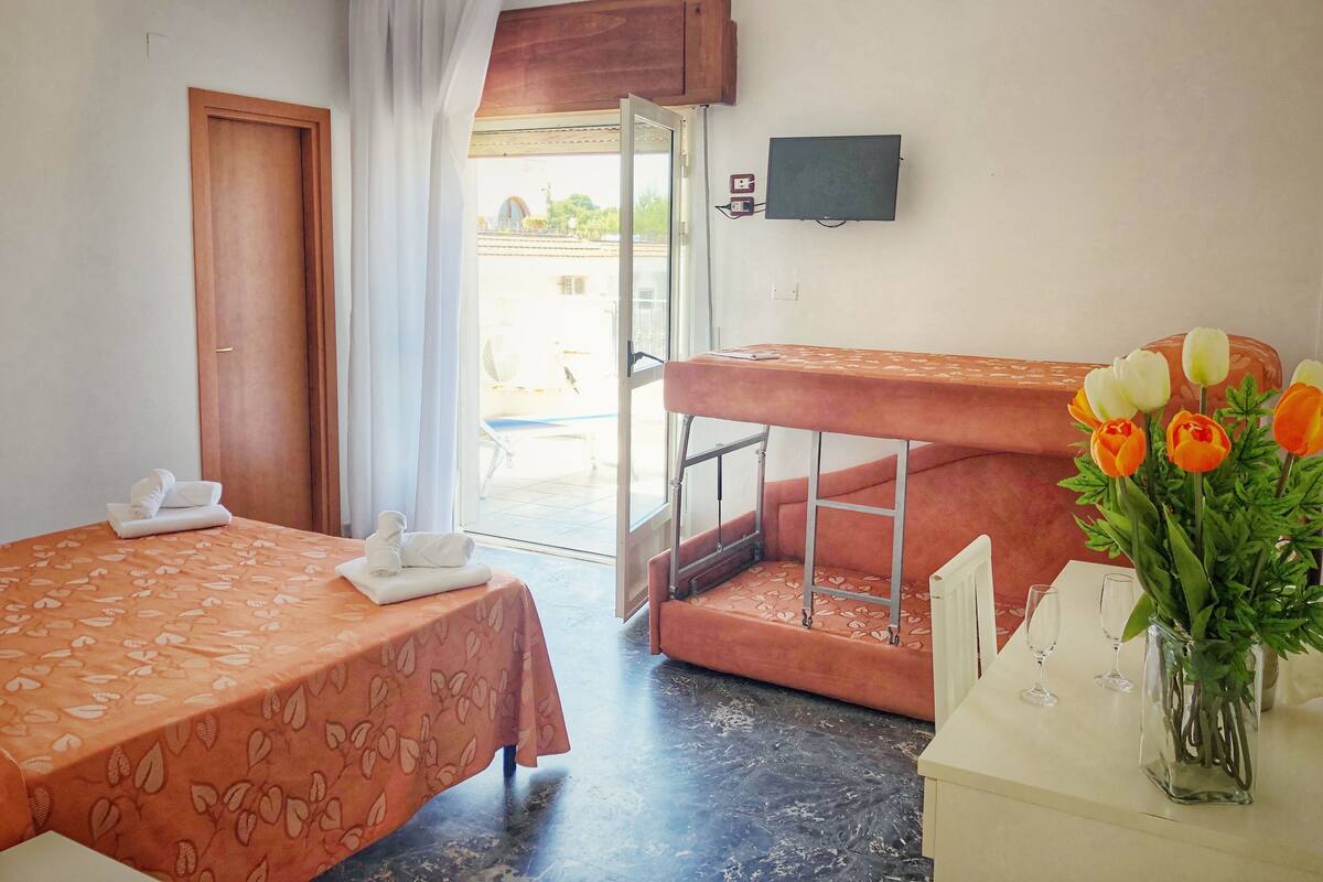 Ein Hotelzimmer mit Bett, kleinem Tisch mit Handtüchern, Balkon mit Aussicht und einer Vase mit Blumen.