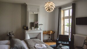 A bedroom with a bed, a desk, a chair, a radiator, and a window with curtains.