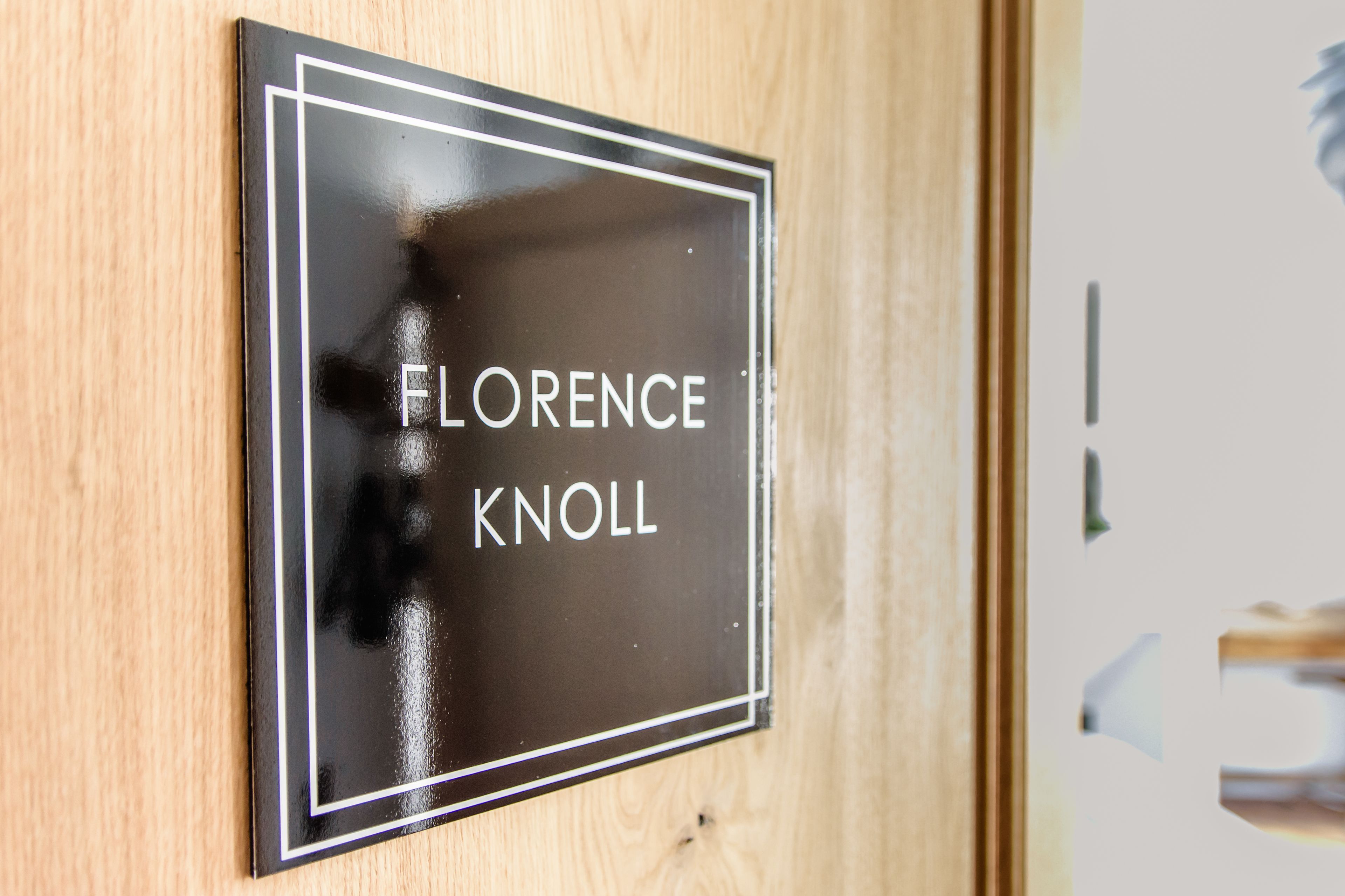 Ein schwarzes Schild mit weißer Schrift auf Holz, beschriftet mit 'FLORENCE KNOLL'.