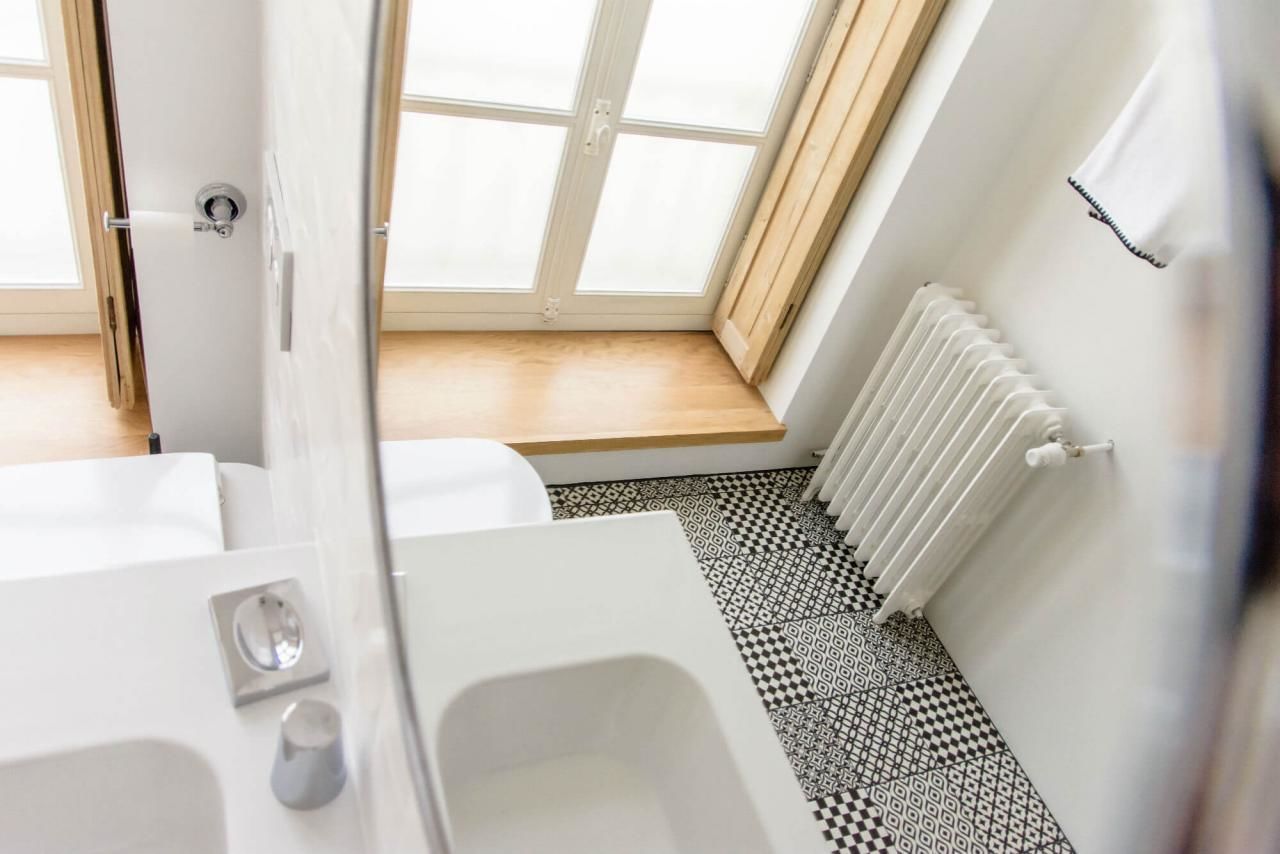 A modern bathroom with a white bathtub, a shower, a toilet, and a window with a wooden floor view.