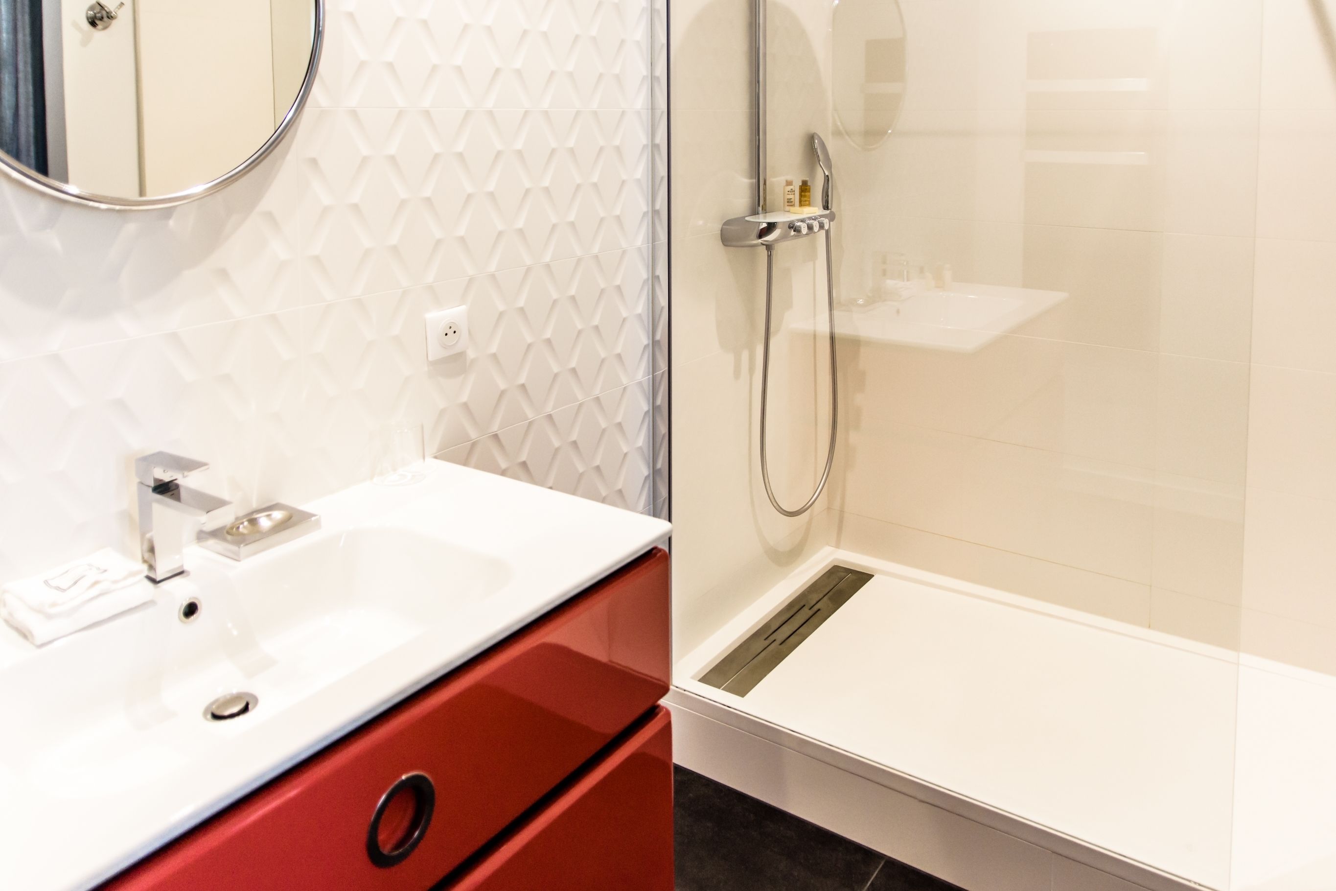 A bathroom with a white sink, red cabinet, and a shower area with a glass door.