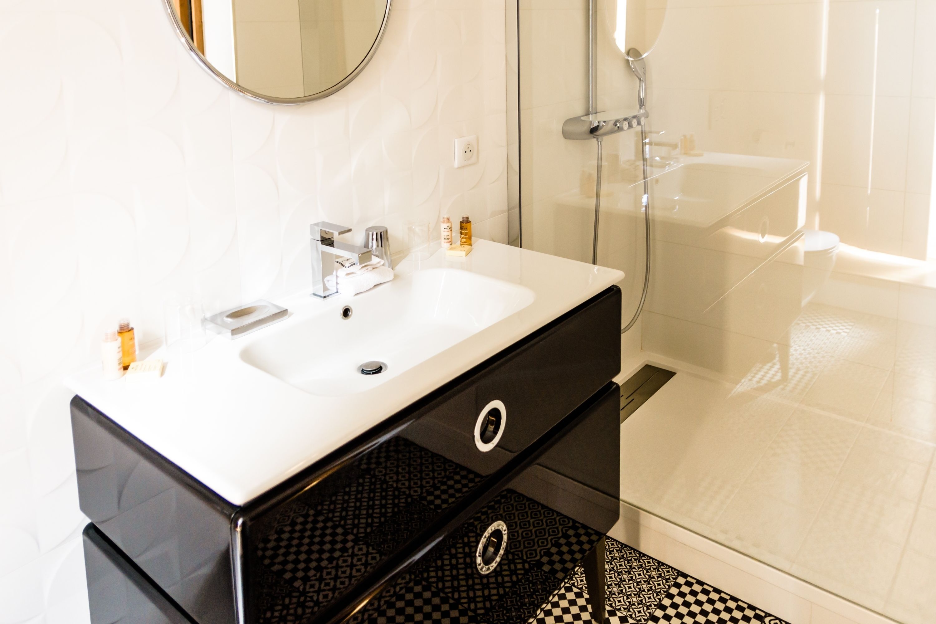 Un baño moderno con un lavamanos blanco, suelo con estampado blanco y negro, y cabina de ducha de vidrio.