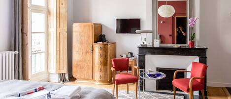Una habitación de hotel con una cama, un armario de madera, una silla roja, una mesita, una chimenea y un televisor montado en la pared.