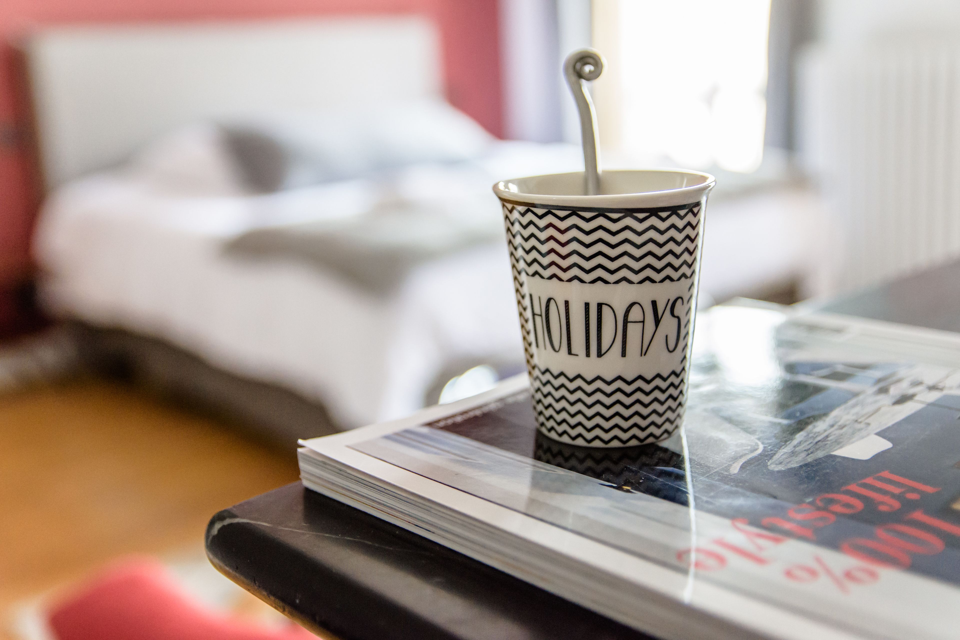 A cup with the word "HOLIDAYS" on it, placed on a table with a magazine.