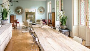 A spacious dining area with a long wooden table, surrounded by chairs, and a large potted plant.