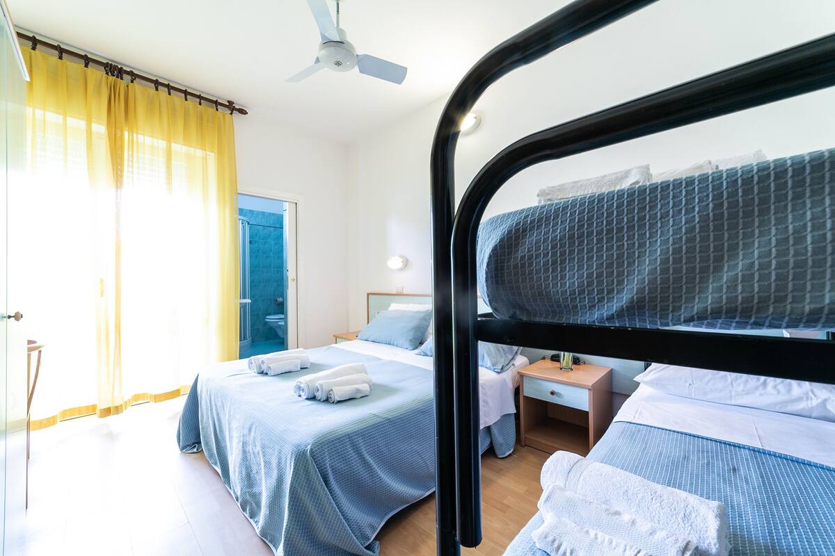 A bedroom with two beds, a ceiling fan, and a bedside table with a lamp.