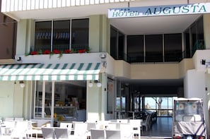 A hotel named "Hotel Augusta" with outdoor seating, a balcony with red flowers, and a view of the sea. - Hotel Augusta (Gabicce Mare)