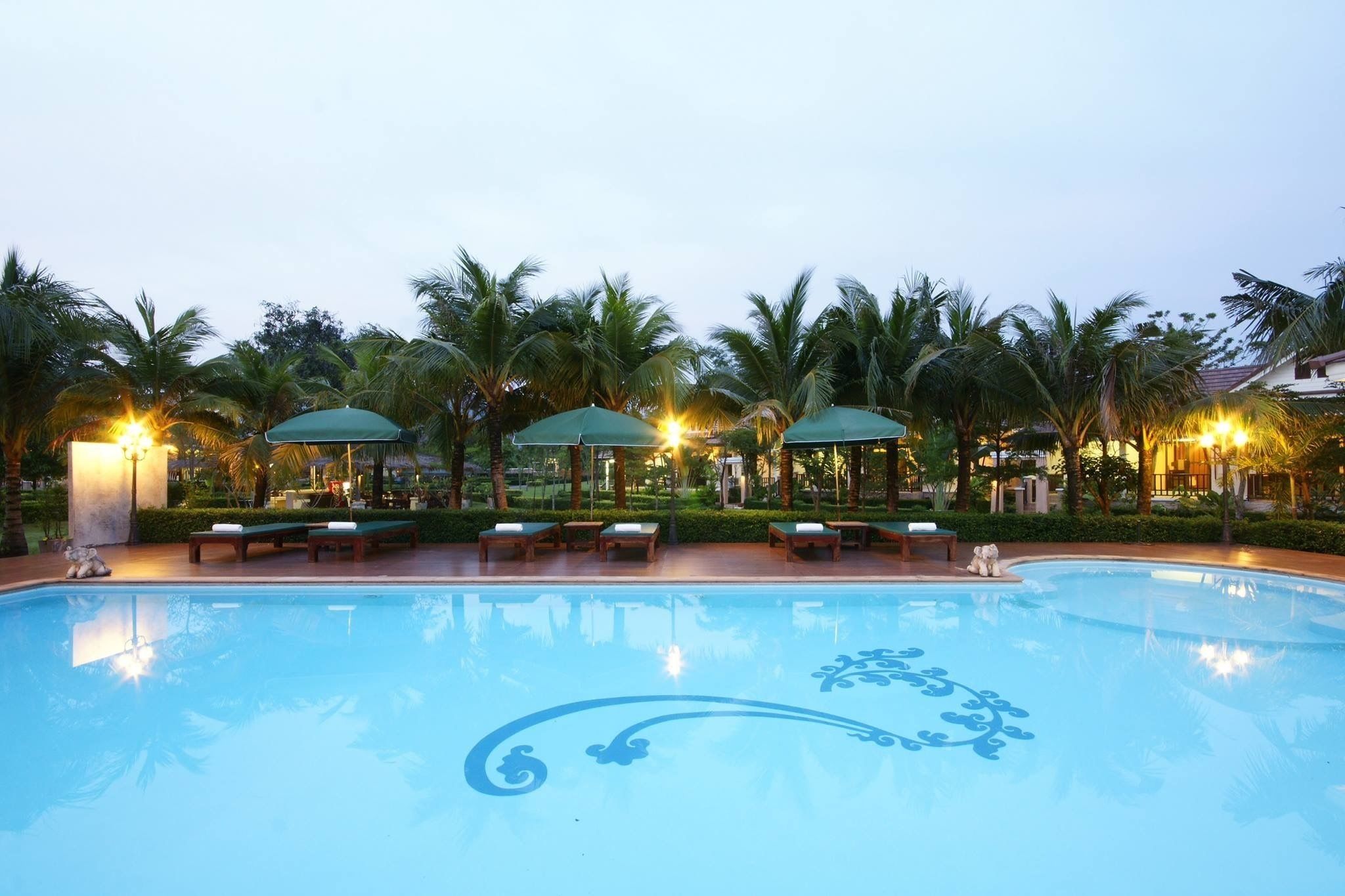 A swimming pool with lounge chairs and umbrellas, surrounded by palm trees.