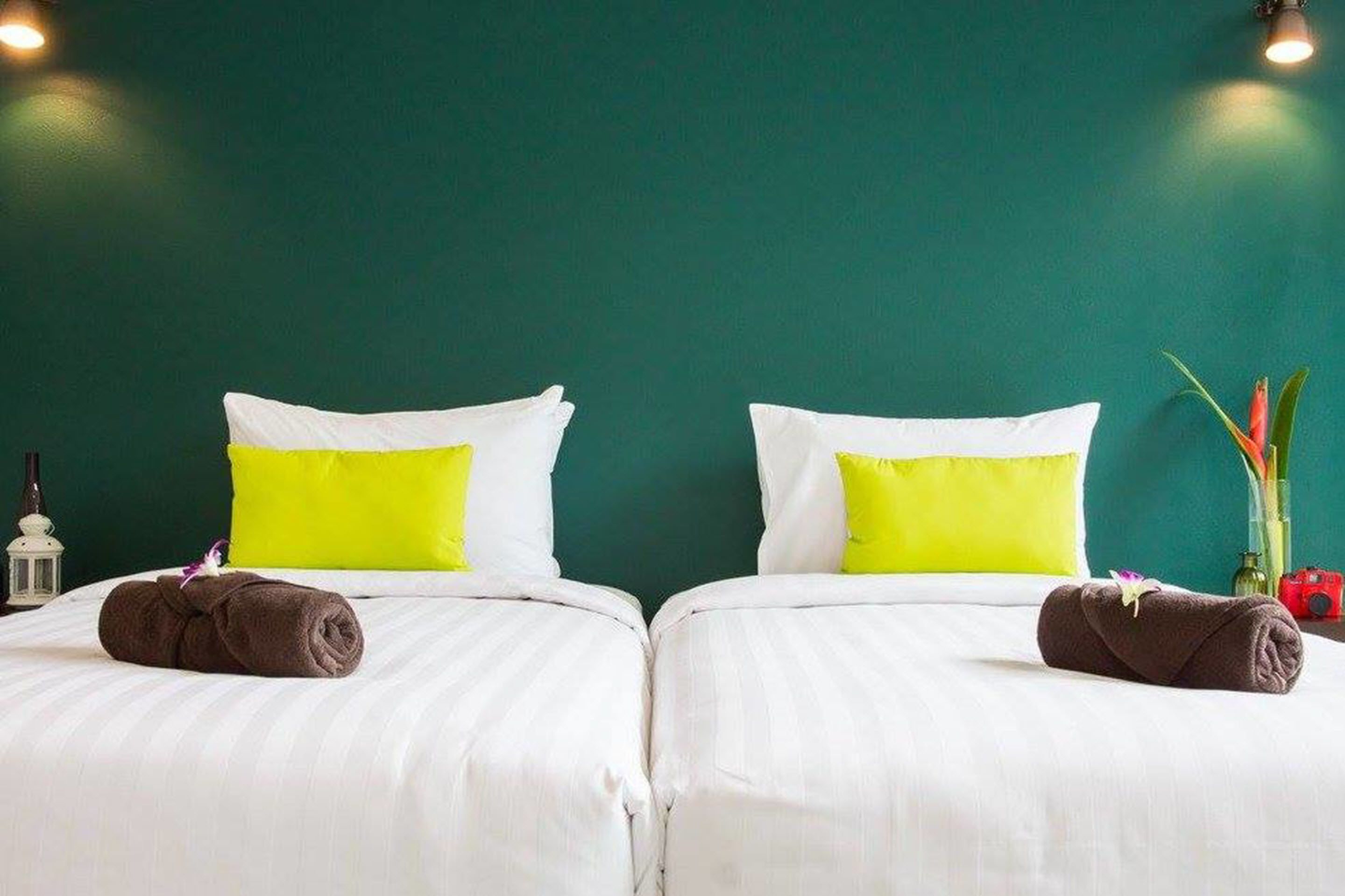 Habitación doble con dos camas, cada una con ropa blanca y un almohadón amarillo brillante.