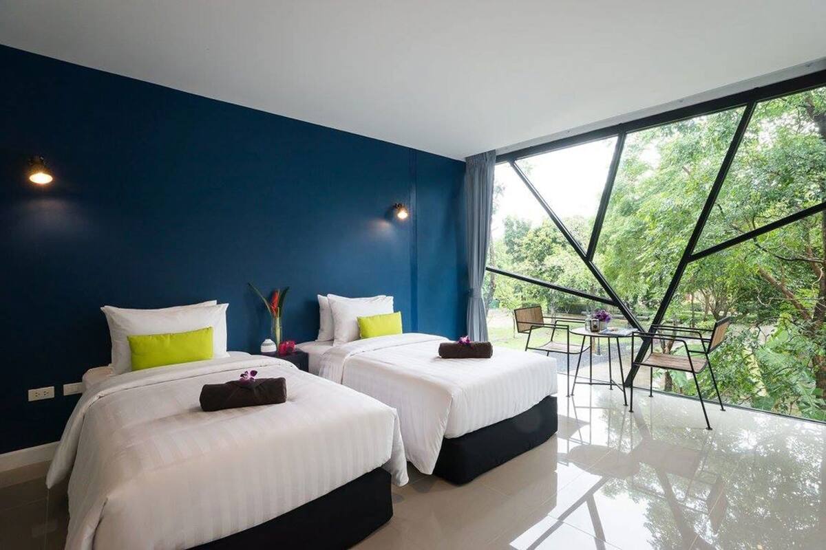 Habitación de hotel moderna con dos camas, un ventanal grande y un balcón con vistas a árboles.
