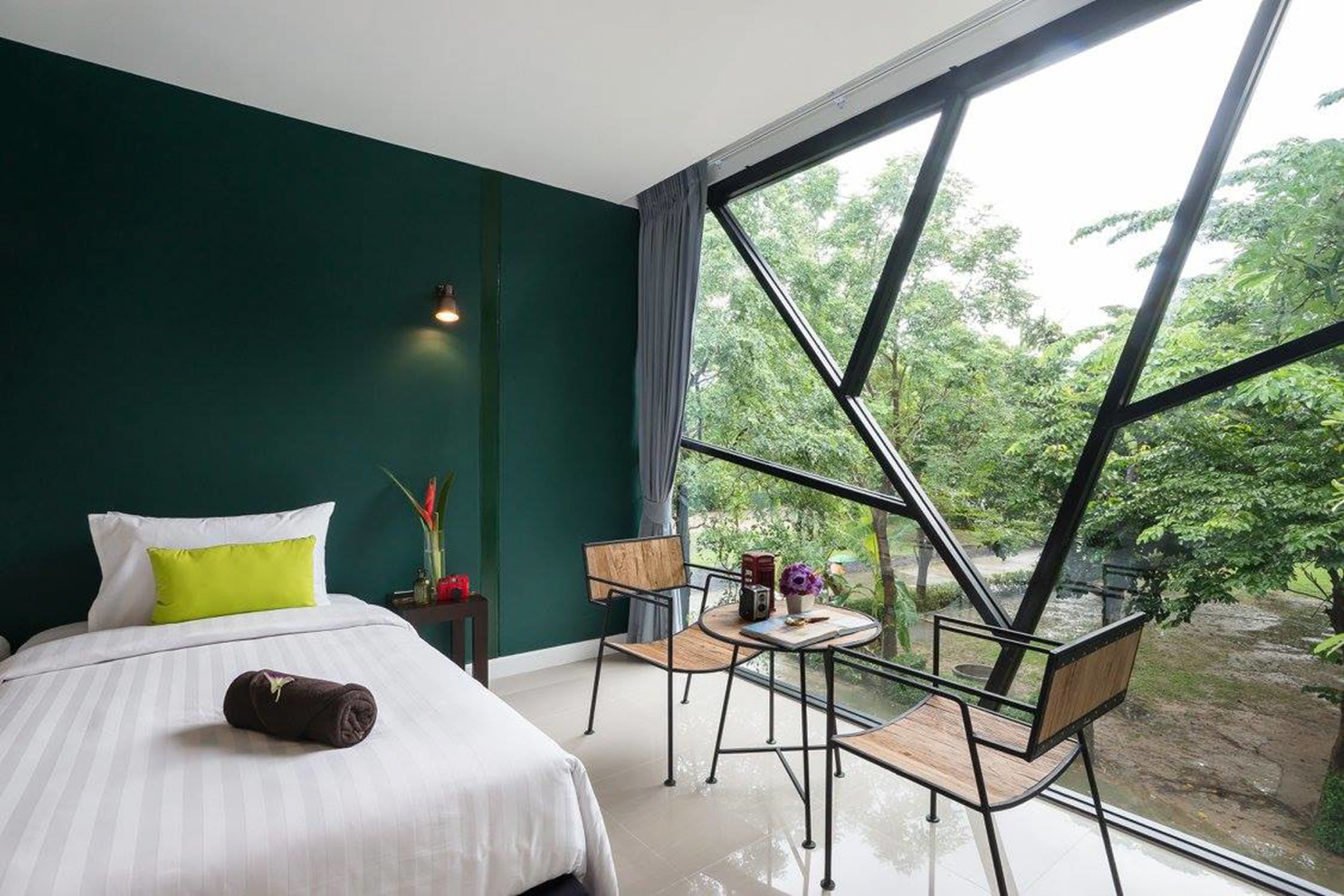 Une chambre à coucher comprenant un lit, une table de chevet, une chaise, une petite table et une grande fenêtre donnant sur un paysage verdoyant.