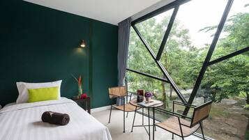 Une chambre à coucher comprenant un lit, une table de chevet, une chaise, une petite table et une grande fenêtre donnant sur un paysage verdoyant.