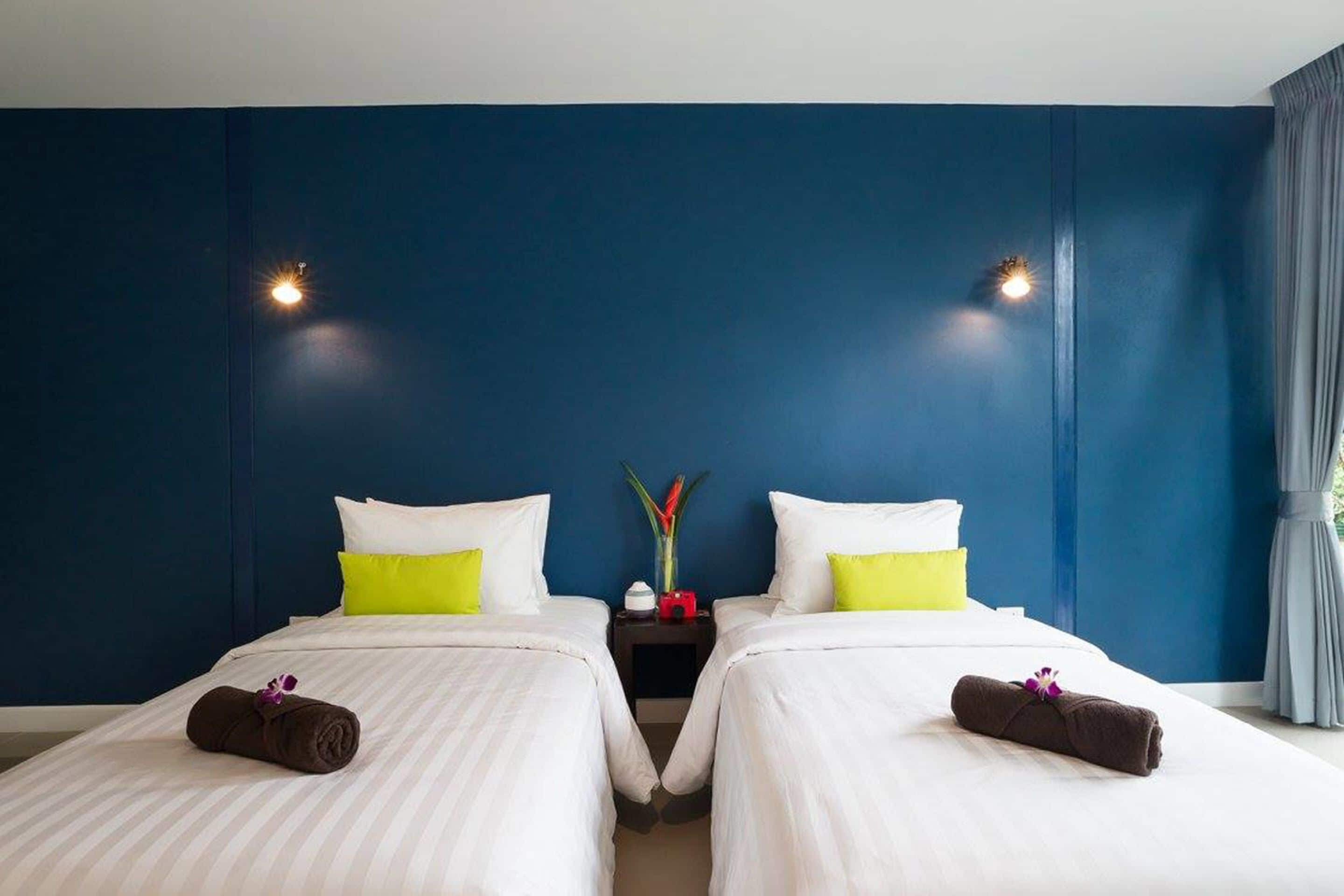Habitación de hotel con dos camas, ropa de cama blanca y una pared de acento azul.