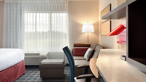 A hotel room with a bed, a desk, a chair, a sofa, a lamp, and a window with curtains.