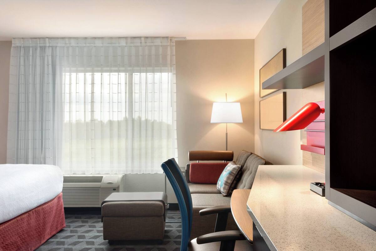 Een hotelkamer met een bed, een bureau, een stoel, een bank, een lamp en een raam met gordijnen.