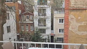 A balcony with a round table and two chairs, overlooking a cityscape with multi-story buildings. - Bufes Hotel (Istanbul)