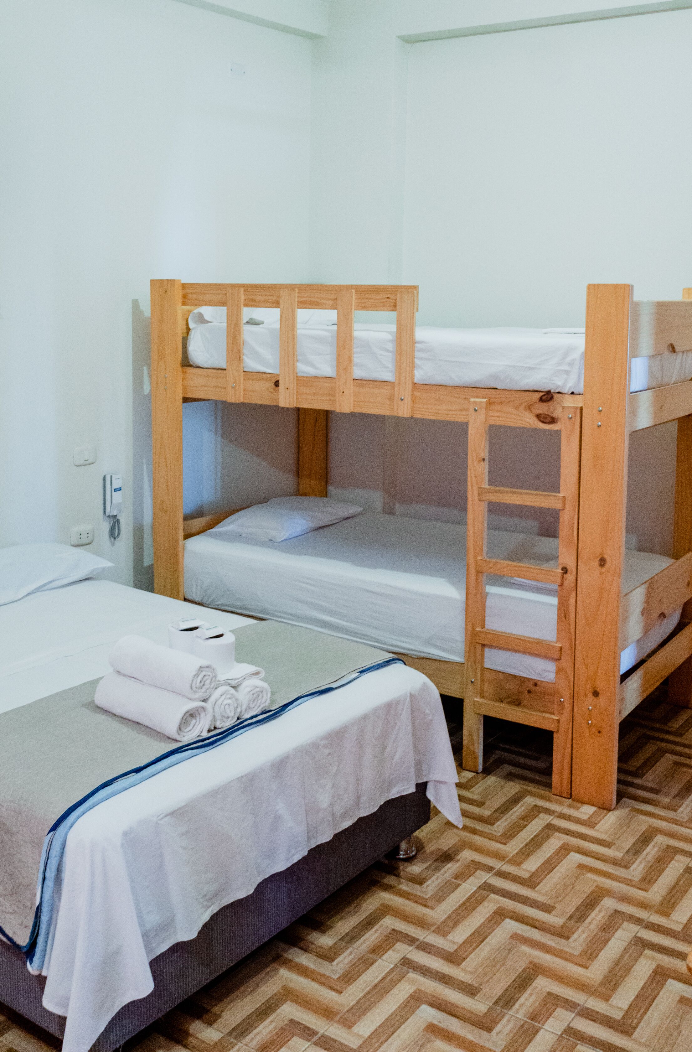 A bunk bed room with a wooden ladder, a desk with a chair, and a telephone.