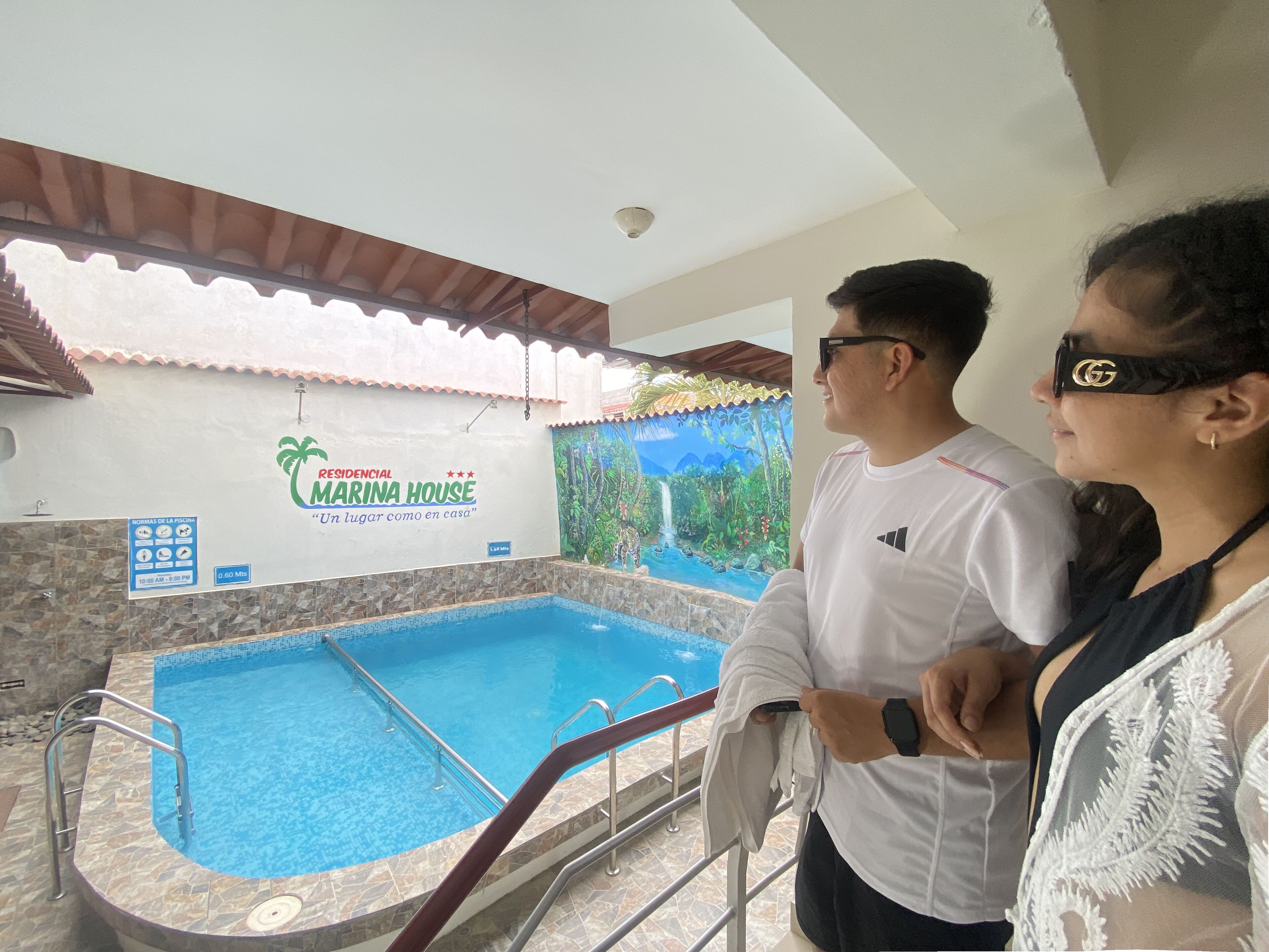 Un espace autour d’une piscine agrémenté d’une enseigne indiquant « RÉSIDENCE MARINA HOUSE » et d’une fresque représentant un paysage tropical.