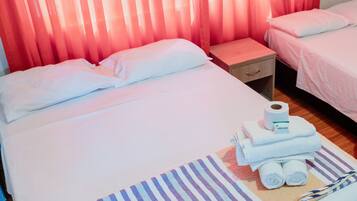 A hotel room with a bed, a nightstand, and a small table. There is a rolled-up towel and a bottle of hand sanitizer on the bed.