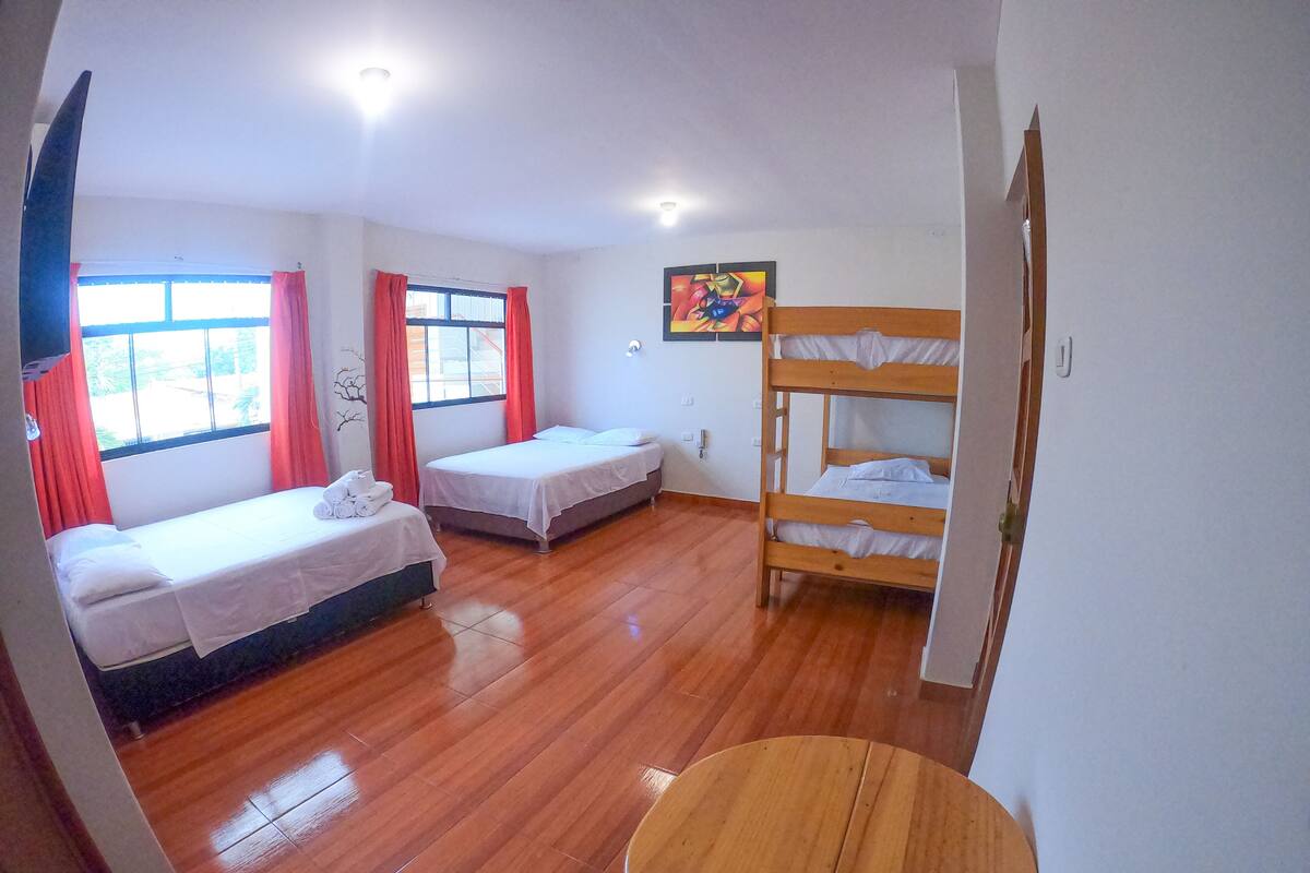 A room with two single beds, a bunk bed, a round wooden table, and a window with curtains.