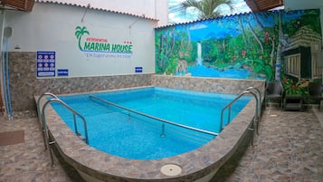 Une piscine ornée d’une fresque représentant une scène de jungle au fond, un panneau indiquant « Résidentiel Marina House », et un sol carrelé autour de la piscine.
