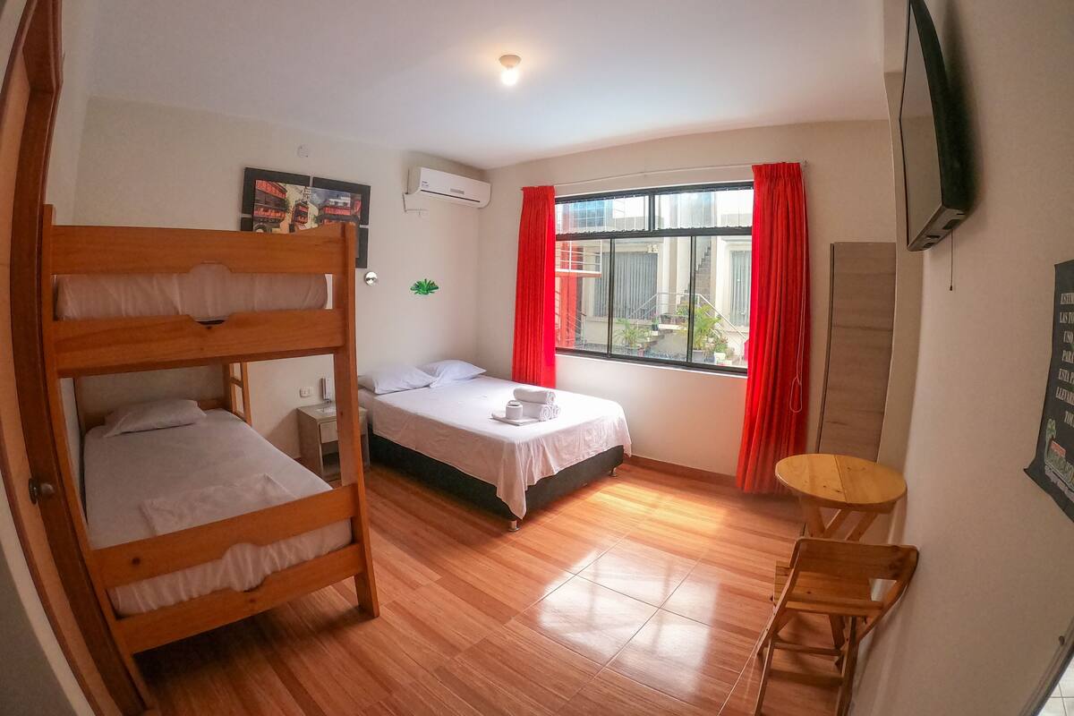 A room with two bunk beds, a single bed, a small table, a TV, and a window with red curtains.