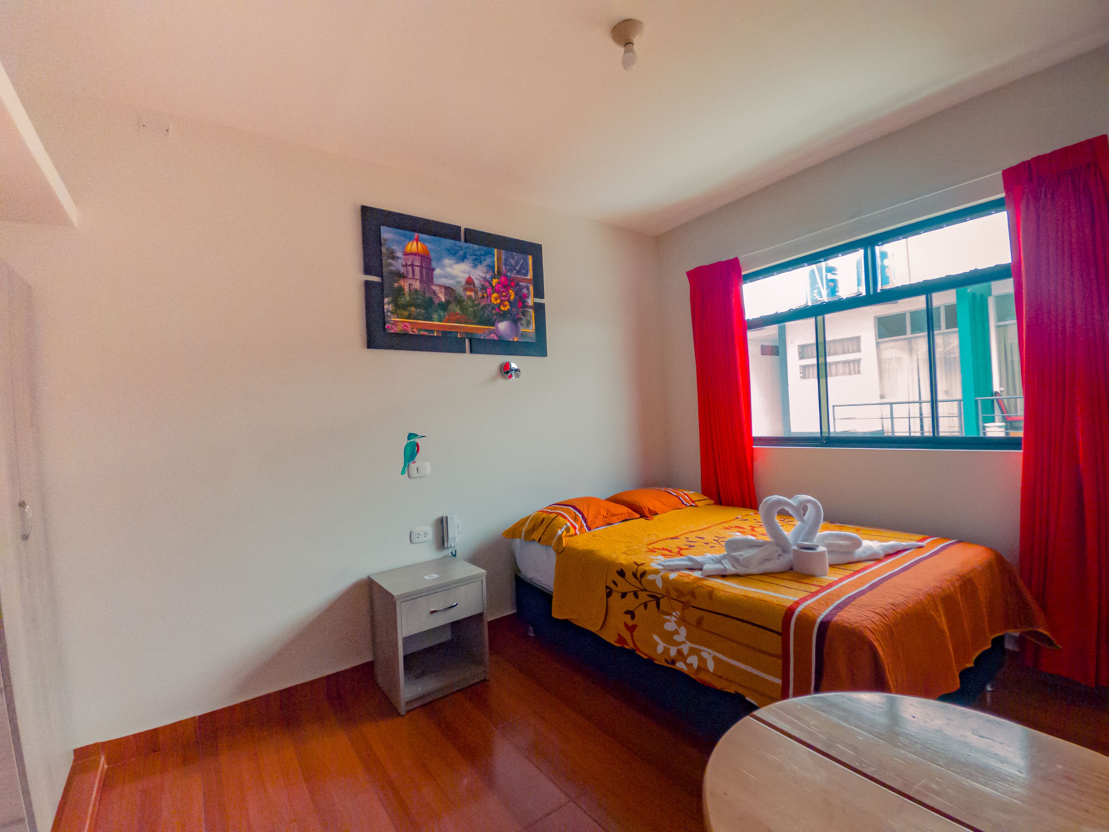 Una habitación de hotel con una cama, una mesita de noche, una ventana con cortinas rojas y un cuadro en la pared.