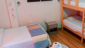 Quarto com duas camas de solteiro, uma cama beliche de madeira, uma pequena mesa de cabeceira com luminária e uma parede com um quadro colorido.