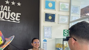 A reception desk with a sign labeled "RECEPTION" and a "RESIDENCIAL MARINA HOUSE" sign. There are framed awards on the wall, a glass display case with snacks, and a "Safe Levels" sign. - Residencial Marina House (La Banda de Shilcayo)