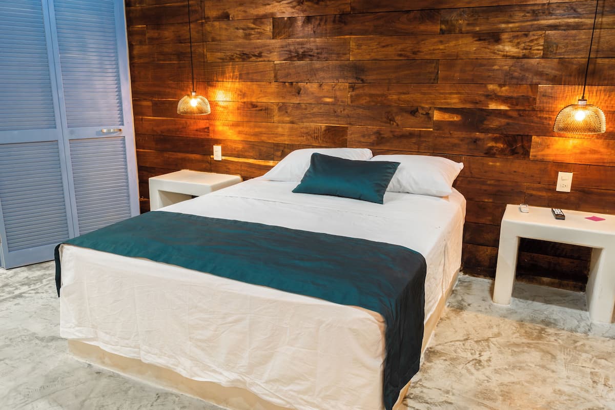 A bedroom with a wooden headboard, a bed with white and teal bedding, two bedside tables with lamps, and a wardrobe with sliding doors.