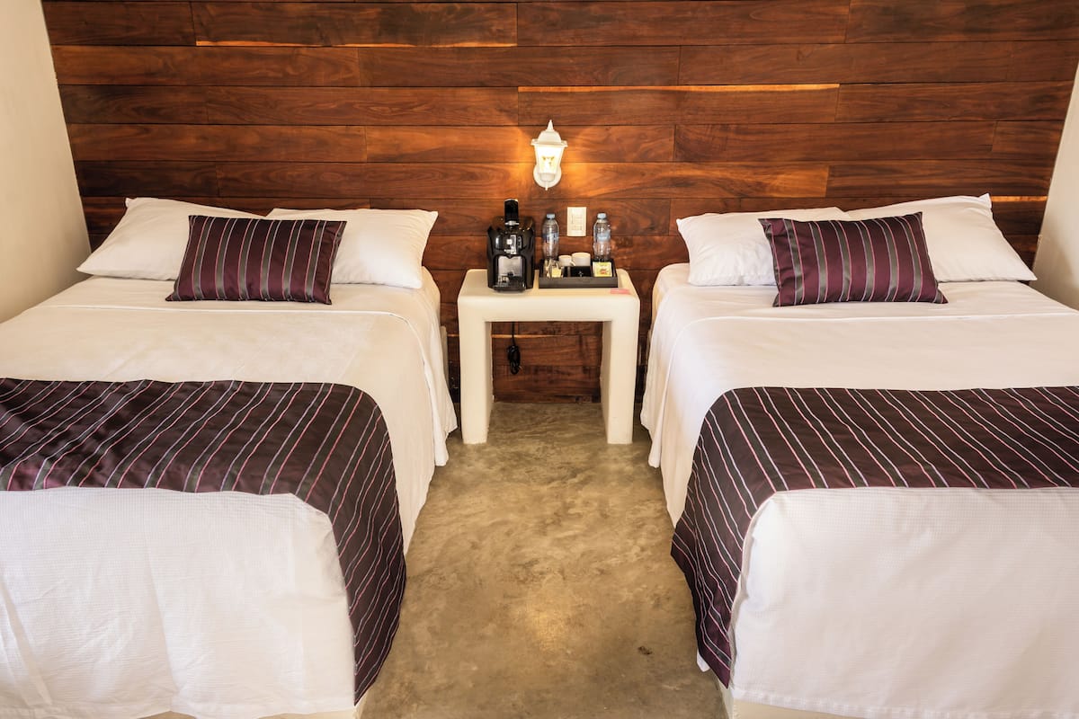 A hotel room with two beds, a nightstand with a coffee maker, and a wooden headboard.