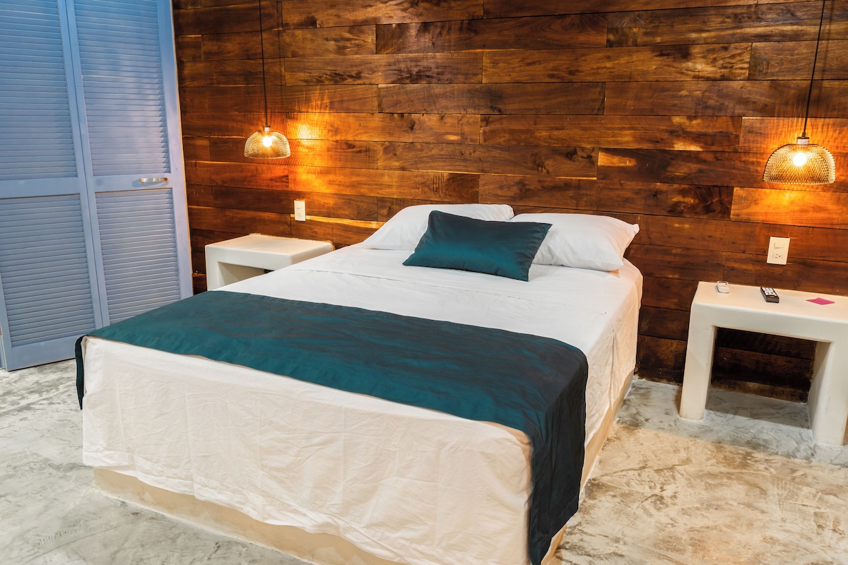A bedroom with a wooden headboard, a bed with white and teal bedding, two bedside tables with lamps, and a wardrobe with sliding doors.
