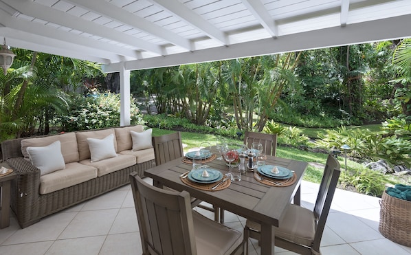 An outdoor patio with a dining table set for four, surrounded by lush greenery.