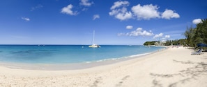 A beach with clear blue water, a sandy shore, and a few boats.