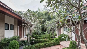A courtyard with a brick pathway, neatly trimmed hedges, and a variety of trees and shrubs. - Wangyao Riverside Resort (Nakhon Nayok)