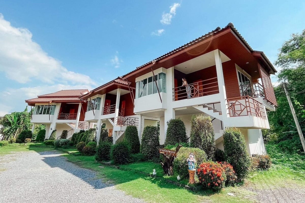 A two-story building with a red roof and white walls, featuring balconies and a gravel driveway.