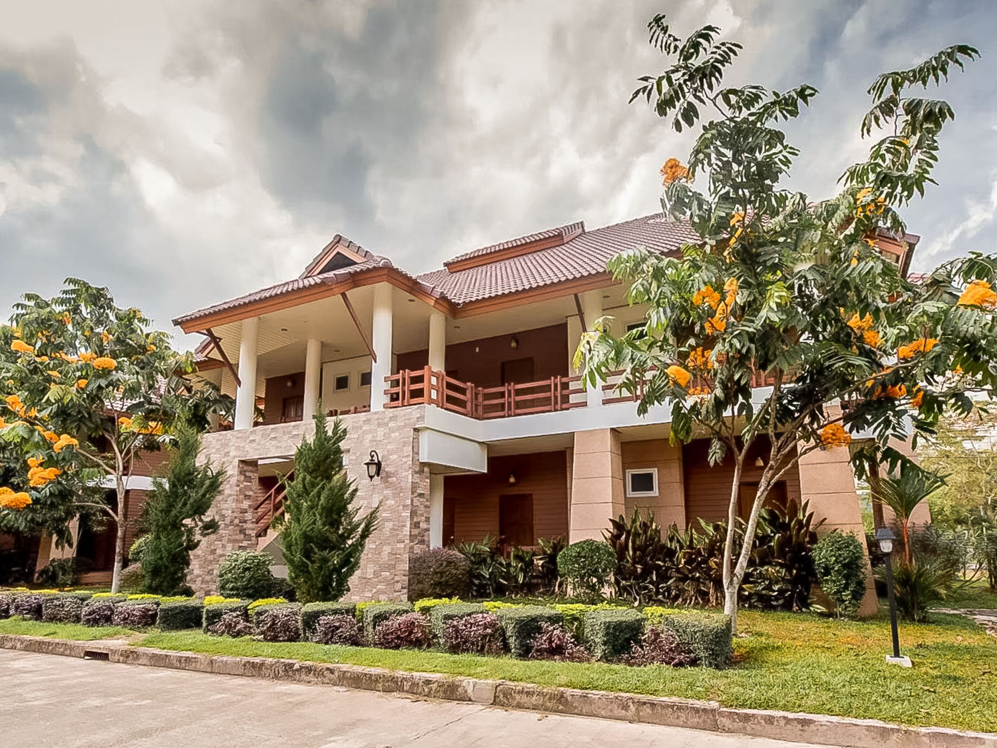 A two-story house with a balcony, surrounded by well-maintained gardens and trees.