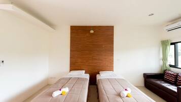 Quarto de hotel com duas camas, uma parede de destaque em madeira, uma janela com cortinas e um sofá de couro.