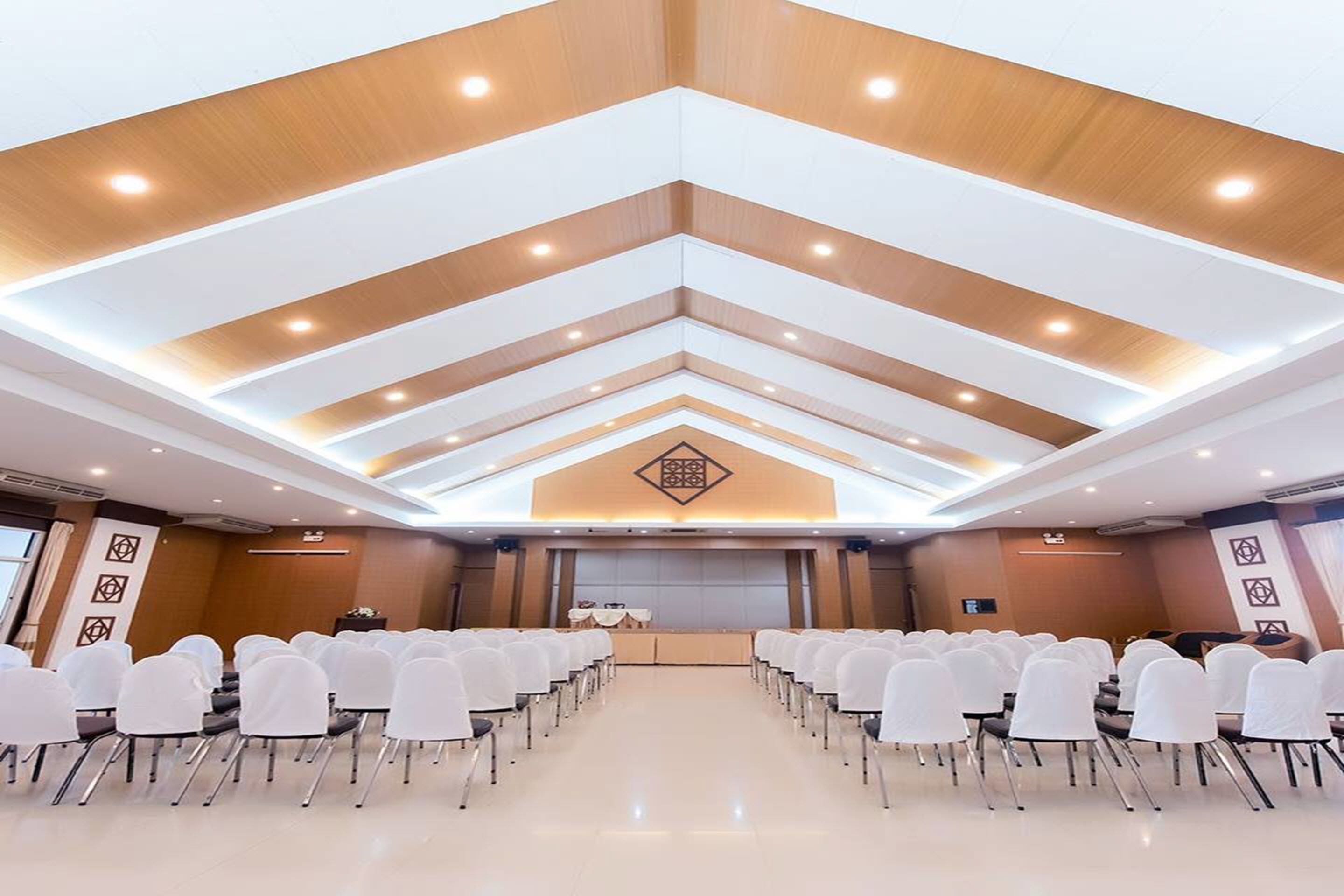 Une salle de conférence avec des rangées de chaises blanches, une scène dotée d’un pupitre et un plafond au design moderne.