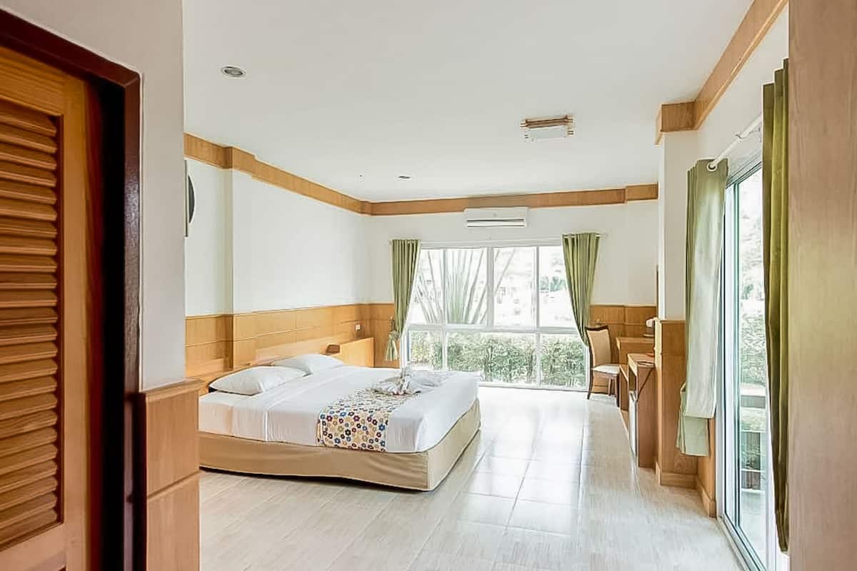 A hotel room with a large bed, a desk, and a view of greenery through the window.