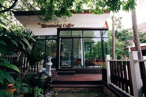 A coffee shop named "The Blooming Coffee" with a wooden exterior and glass doors.