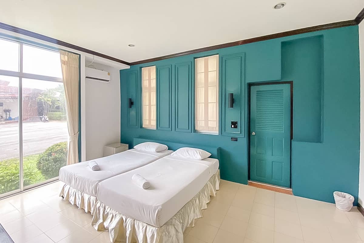 A room with two beds, a teal-colored wall, a window with curtains, and a door.