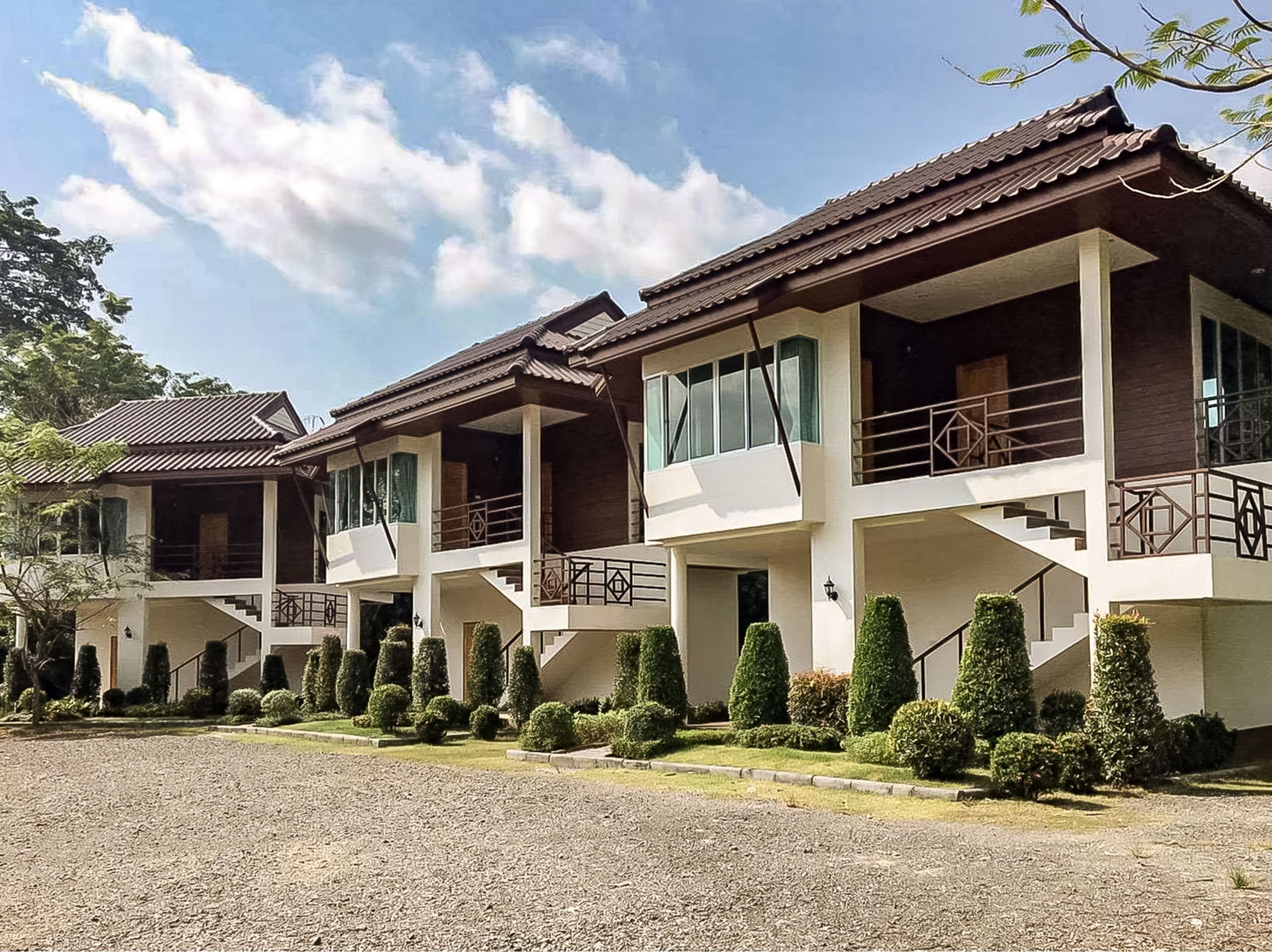 A row of two-story buildings with balconies, a gravel driveway, and neatly trimmed hedges.
