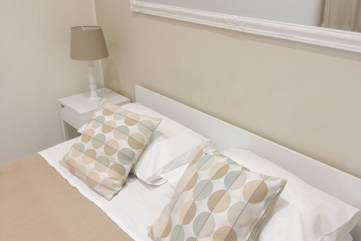 A neatly made bed with two pillows, a bedside table with a lamp, and a mirror above the bed.