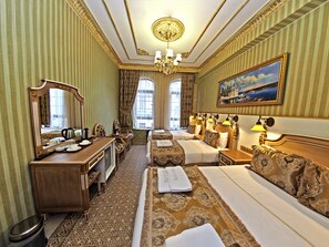 A hotel room with two beds, a desk, a mirror, a chandelier, and a painting on the wall.