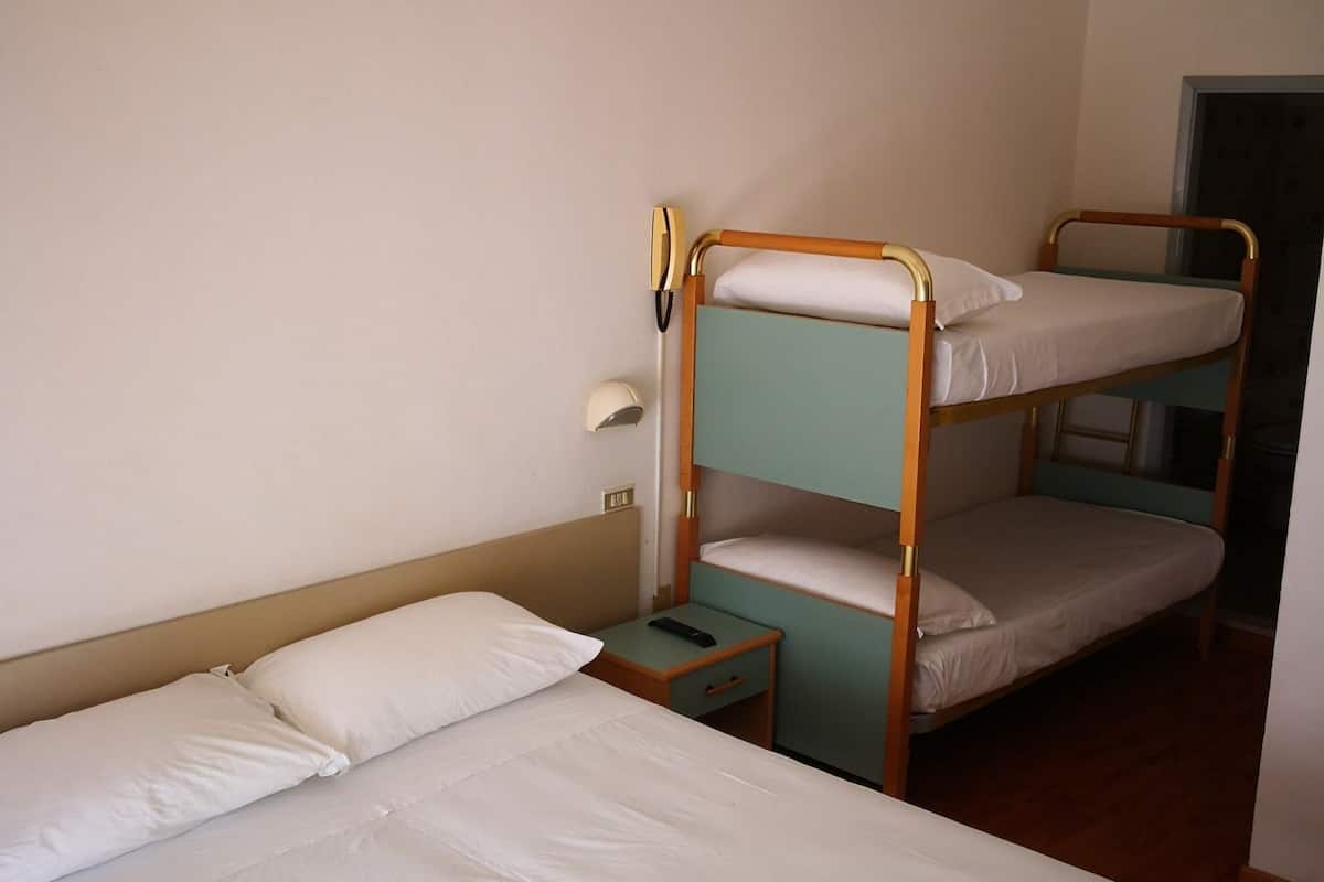 Habitación con literas, una cama individual a la izquierda y una litera a la derecha. Hay una mesita de noche con una lámpara y una pequeña mesa junto a la cama individual.