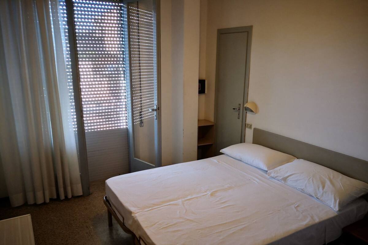 Un dormitorio con cama, puerta y ventana con persianas.